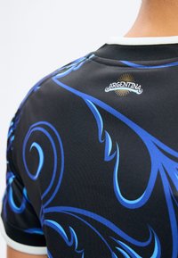 Svart sportsdrakt med blå virvlende mønstre og en liten "Argentina" tekstlogo med en solstråle over øvre bakhalsen.