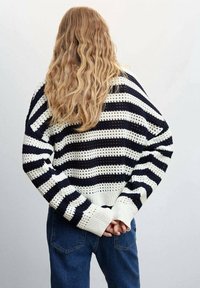 Gestrickter Pullover mit marineblauen und weißen horizontalen Streifen, weiten Ärmeln, gerippten Bündchen und einer offenen Strickstruktur, kombiniert mit blauen Jeans.