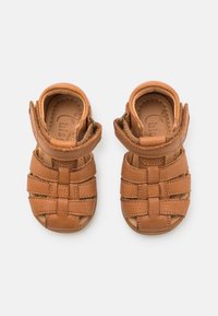 Braune Leder-Sandalen mit offenen Zehen, ausgestattet mit überkreuzten Riemen und einem Klettverschluss am Knöchel. Strukturierte Oberfläche für besseren Halt.