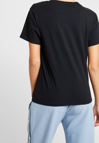 Svart bomull t-shirt med korta ärmar, rund halsringning och en slät struktur, visad från baksidan med ljusblå byxor.