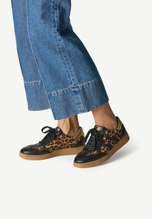 Schoenen met luipaardprint voorzien van zwarte leren accenten, een gestructureerde zool, zwarte veters en gouden hardware, gecombineerd met korte denim broek.