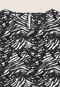 Top à motifs noir et blanc avec un design en forme de vague, fabriqué en tissu léger, avec un décolleté en V et une fermeture à bouton à l'arrière.