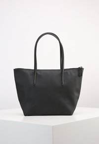 Schwarze Tragetasche aus strukturiertem Nylon, mit zwei langen Griffen und einem Reißverschlussverschluss. Einfache, rechteckige Form mit minimalem Design.