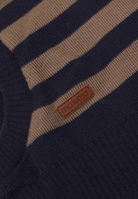 Sweter w paski w kolorze granatowym i beżowym z wzorem teksturowanym. Posiada brązową skórzaną metkę z haftowanym logo "maximo".