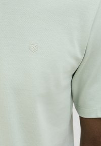 Lichtgroen poloshirt van gestructureerde stof, met een klein, geborduurd embleem op de borst en korte mouwen.