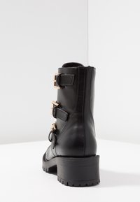 Stivaletto alla caviglia in pelle nera con tre cinturini regolabili e fibbie color oro. Punta arrotondata e suola spessa e strutturata. Superficie superiore liscia.