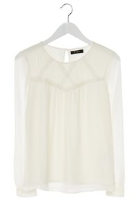 Bílá dlouhá průhledná blůza s nabíraným horním dílem a dekoračními křížkovými stehy, visící na bílém ramínku.