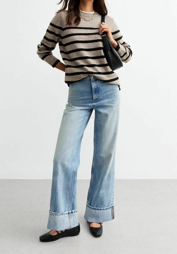 Stribet striktrøje i beige og sort, højtaljede lys blå jeans med brede ben og opkrøllede manchetter, parret med sorte slip-on sko.