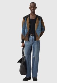 Υφασμένο ζακέτα με μπλε, καφέ και μαύρα διαμαντένια σχέδια, συνδυασμένο με ανοιχτό μπλε τζιν με ξεβάμματα και μαύρη τσάντα ώμου. Μαύρα παπούτσια.