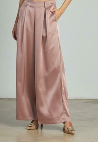 Helle rosa Satin-Hosen mit weitem Bein, Frontfalten, hoher Taille und glatter Textur, kombiniert mit verzierten beigen Schuhen.