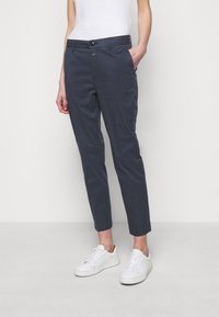 Marina chinos med skräddarsydd passform, sidofickor och en enkel knappstängning, i kombination med vita sneakers. Tyget verkar slätt och hållbart.