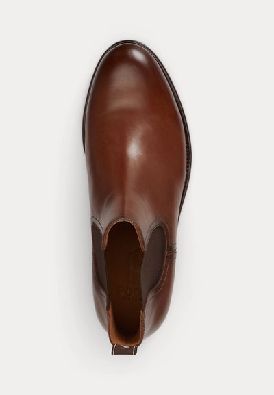 Καφέ δερμάτινο Chelsea μπότες τύπου slip-on με ελαστικά πλαϊνά πάνελ και ταινία έλξης, εμφανίζεται από πάνω σε λευκό φόντο.