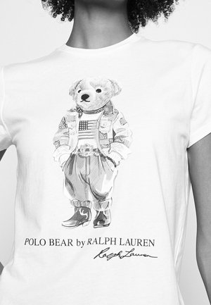 Ours en peluche portant un t-shirt imprimé du drapeau américain, une veste, des bottes et un pantalon, avec le texte "POLO BEAR by RALPH LAUREN" en dessous.