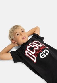 Čierne bavlnené tričko s odvážnym bielym a červeným grafickým dizajnom s textom "DCSHOE COMPANY EST. 094", voľný strih, okrúhly výstrih.