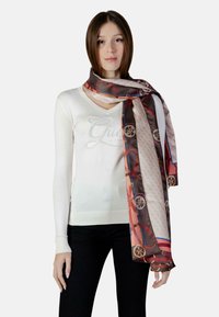 Sciarpa di seta con un mix di motivi marroni, rossi e beige con accenti circolari, elegantemente drappeggiata intorno al collo di una modella.