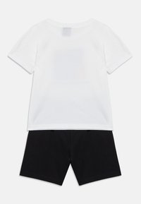 Λευκό βαμβακερό μπλουζάκι με κοντά μανίκια και στρογγυλή λαιμόκοψη, σε συνδυασμό με μαύρο βαμβακερό σορτς. Απλός σχεδιασμός, χωρίς ορατά σχέδια ή μεταλλικά στοιχεία.