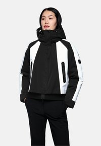 Schwarze und weiße Jacke mit Kapuze, cropped geschnitten, mit Reißverschluss-Taschen, kontrastierendem Panel-Design und elastischen Bündchen. Glatte Stoffoberfläche.