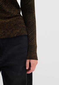 Top nero a maniche lunghe con un motivo a onde dorate strutturato, abbinato a pantaloni neri testurizzati. Il tessuto sembra morbido, con maniche aderenti.
