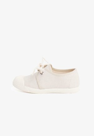 Beżowe płócienne trampki z zaokrąglonym czubkiem, białą gumową podeszwą i teksturowanymi detalami. Posiada bawełniane sznurówki i metalowe oczka do zapinania.