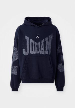 Námornícky modrá mikina s kapucňou s grafickým nápisom "JORDAN" v sivej farbe, logom na hrudi a textúrovanými akcentmi na rukávoch. Vyrobená z bavlny, s prednou vreckom.