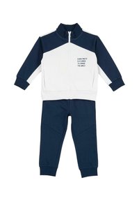 Survêtement bleu marine et blanc comprenant une veste zippée à col montant avec texte imprimé, assortie à un pantalon à jambes fuselées.