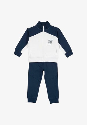 Marineblaue und weiße Trainingsanzug aus einer Jacke mit Reißverschluss und hohem Kragen mit aufgedrucktem Text, kombiniert mit passenden Hosen mit zulaufenden Beinen.