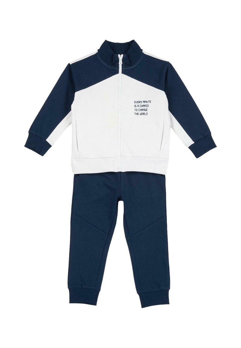 Survêtement bleu marine et blanc comprenant une veste zippée à col montant avec texte imprimé, assortie à un pantalon à jambes fuselées.