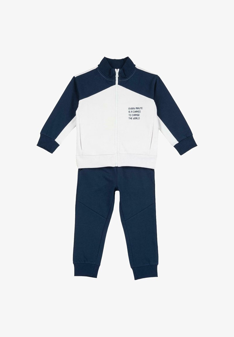 Survêtement bleu marine et blanc comprenant une veste zippée à col montant avec texte imprimé, assortie à un pantalon à jambes fuselées.