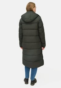 Lang, grøn pufferjakke med hætte, syede paneler og lynlåsdetaljer. Båret med blå jeans og sorte støvler, set fra ryggen.