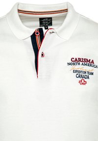 Hvid polo skjorte med en marineblå og rød knapstolpe. Har broderet tekst: "CARISMA NORTH AMERICA" og et canadisk ahornblad. Knapdetalje inkluderet.