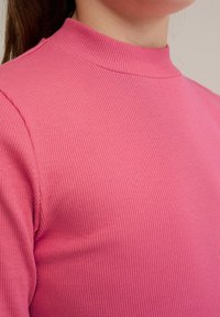 Närbild av en rosa ribbad långärmad topp med hög halsringning och mjuk textur, med horisontella ränder över tyget.