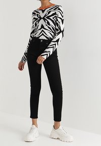 Jeans negros de tiro alto combinados con un suéter a rayas blancas y negras con un cuello naranja. El modelo lleva zapatillas gruesas blancas.