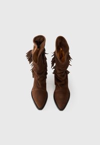 Bottes ankle en suède marron avec un design décontracté, bout pointu et des franges sur les côtés. Semelle en caoutchouc noir. Intérieur doublé.