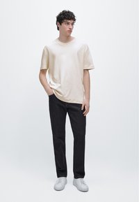 Beige bomullst-shirt med avslappnad passform, kombinerad med mörka jeans i denim. Vita sneakers fulländar outfiten, med en enkel design utan mönster.