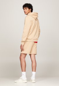 Beige hettegenser med snor og matchende shorts, kombinert med hvite sneakers og sokker. Shortsene har en liten logo på siden.