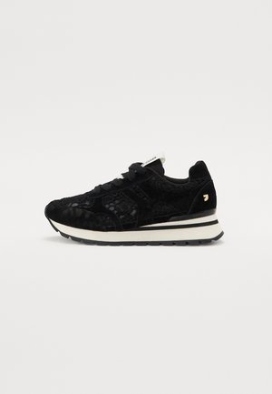 Zapatilla negra con cordones y textura de ante, con una media suela blanca, suela negra y un pequeño acento dorado en el talón.
