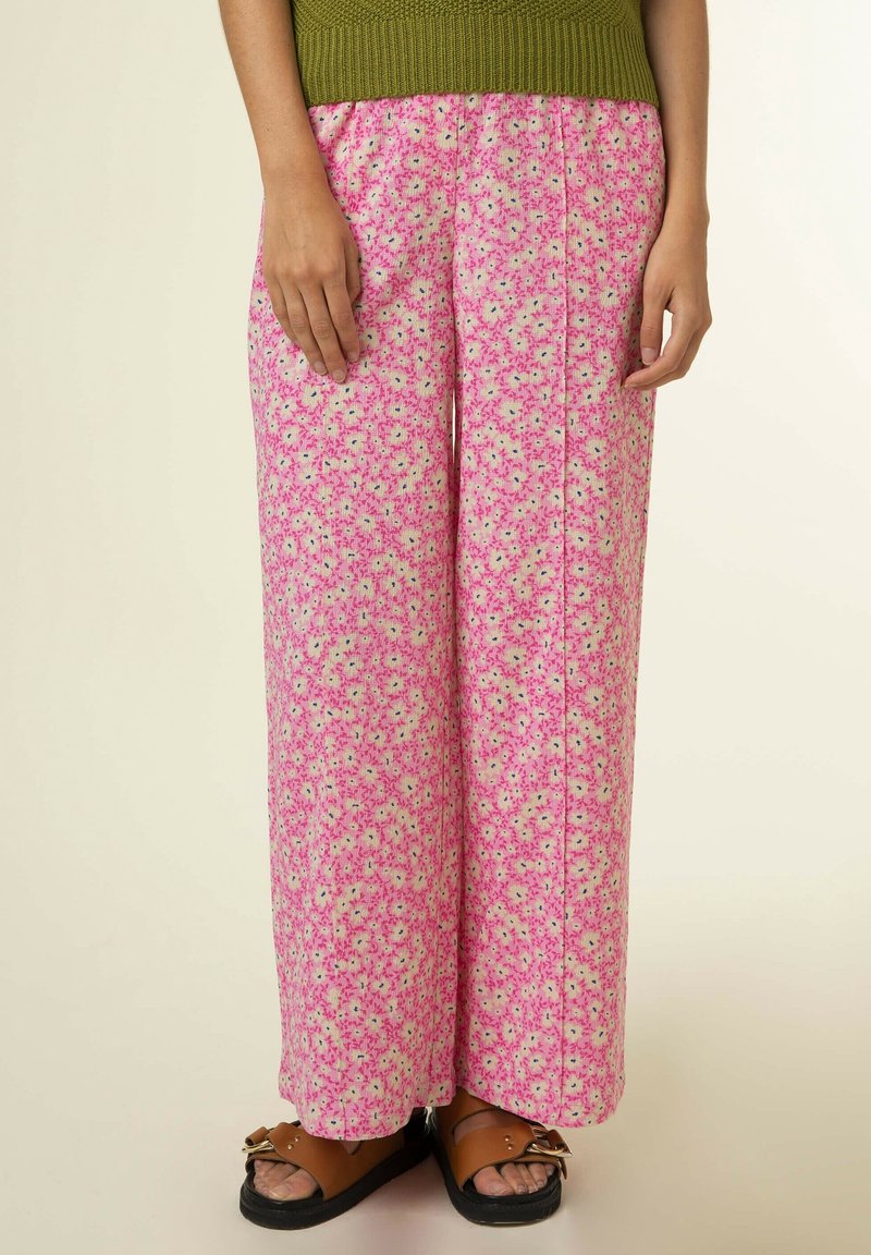 Vida byxor i rosa med ett blommönster som har små vita och blå blommor. Tillverkade av ett lätt tyg med en texturerad yta.