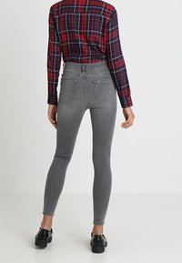 Jeans ajustados de talle alto en gris con una textura suave, dos bolsillos traseros, combinados con una camisa de cuadros roja y zapatos negros.