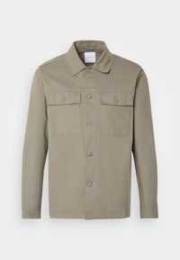 Veste-chemise à manches longues marron clair avec deux poches poitrine boutonnées et un col pointu sur fond blanc.