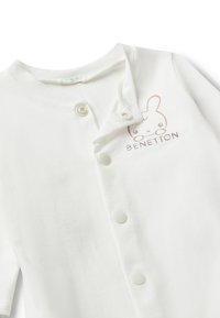 Un body de algodón blanco con cuello de solapa, textura suave y un logo de conejo beige con "BENETTON" impreso debajo. Cierre con botones claros.