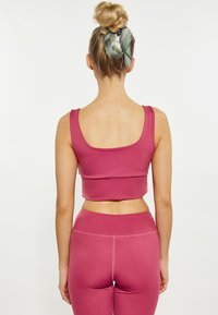 Reggiseno sportivo rosa aderente con spalline larghe e schiena a forma di scollo, abbinato a leggings a vita alta coordinati, entrambi realizzati in materiale liscio ed elasticizzato.