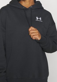 Felpa nera con cappuccio e cordino, realizzata in tessuto morbido. Presenta un logo bianco di Under Armour sulla parte superiore sinistra.