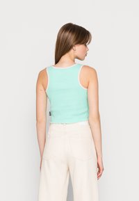 Top cropped em verde menta com detalhes em rosa, apresentando uma bainha em formato de onda. Combinado com calças largas em creme, mostrando a vista de trás.