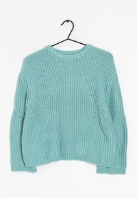Jasnoniebieski sweter z dzianiny o ryżowej fakturze, okrągły dekolt, opadające ramiona i luźny krój. Wisi na czarnym metalowym wieszaku.