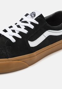 Svarta Vans-sneakers med vit sidosträng, vita snörning, gummisula och Vans Off The Wall-logga på tungan.