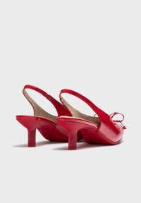Escarpins à talon slingback en cuir verni rouge avec un bout arrondi, un talon bloc de 6 cm et un détail en nœud à l'avant, présentant une finition lisse et brillante.