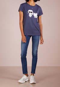 Camiseta de algodón azul marino con personajes de dibujos animados que llevan gafas de sol y un oso, complementada con gráficos de estrellas. Combinada con jeans azules y zapatillas blancas.