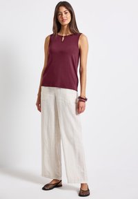 Burgundy ärmlös topp med en nyckelhålsdetalj, tillsammans med lösa vita linbyxor och svarta platta sandaler. En enkel, avslappnad outfit.