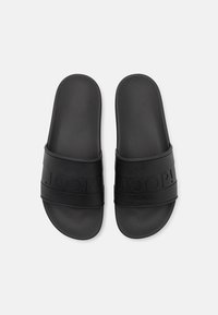 Černé gumové nazouvací sandály se strukturovaným svrchním materiálem, na popruhu s reliéfním logem "JOOP!". Hladká stélka s křivkovým tvarem.