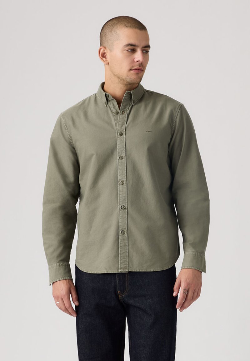 Πουκάμισο σε ανοιχτό ελαιόχρωμο με κουμπιά, από απαλό βαμβακερό ύφασμα, με γιακά τύπου spread, μακριά μανίκια και διακριτική λεπτομέρεια λογότυπου.